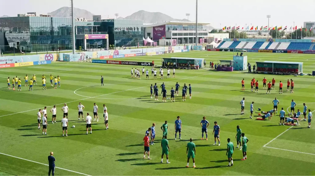 Multiple national teams training simultaneously at adjacent World Cup facilities with different coloured kits